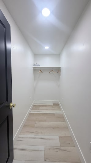 Un pasillo estrecho con suelo de madera, paredes blancas y una puerta a la izquierda.