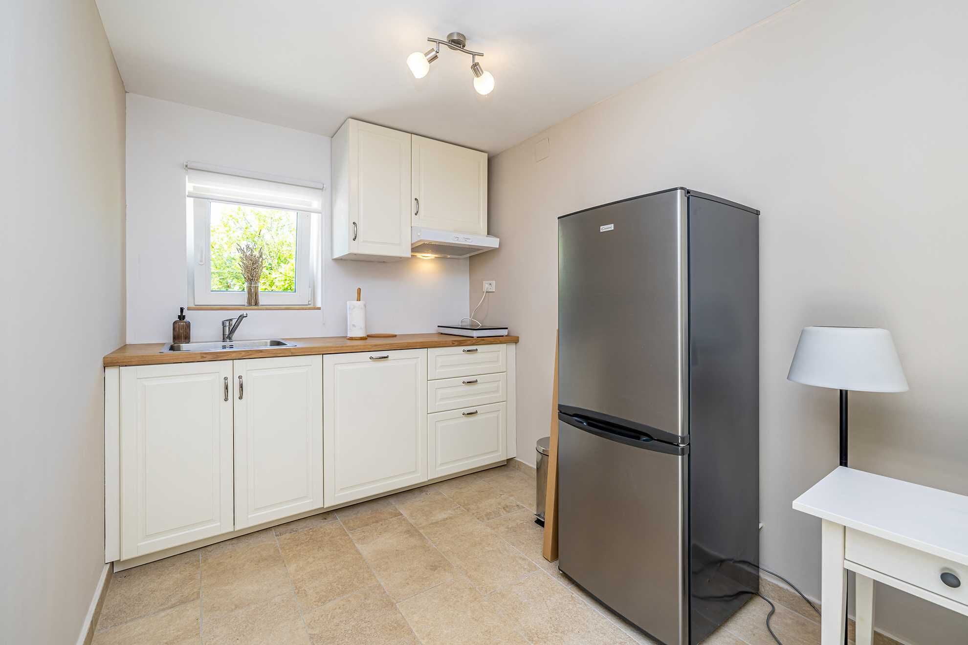 A modern kitchen with white cabinets, a stainless steel refrigerator, and a window with a view of greenery.