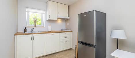 A modern kitchen with white cabinets, a stainless steel refrigerator, and a window with a view of greenery.