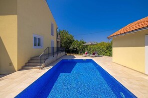 A swimming pool with a tiled deck, a staircase leading to a building, and two lounge chairs with an umbrella. - Holiday house VILLA OLIVA with pool (Poljica)
