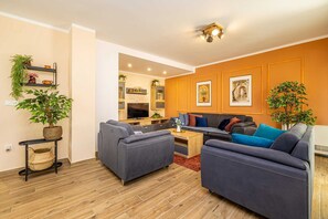 Ein modernes Wohnzimmer mit grauen Sofas, einem Holztisch und einer Küche im Hintergrund.