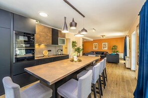 Eine moderne Küche mit einer zentralen Kochinsel, Pendelleuchten an der Decke und einem Essbereich mit einer Couch und Stühlen.