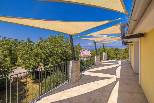 Ein Balkon mit Blick auf Bäume und ein Haus, beschattet durch große Stoffmarkisen.