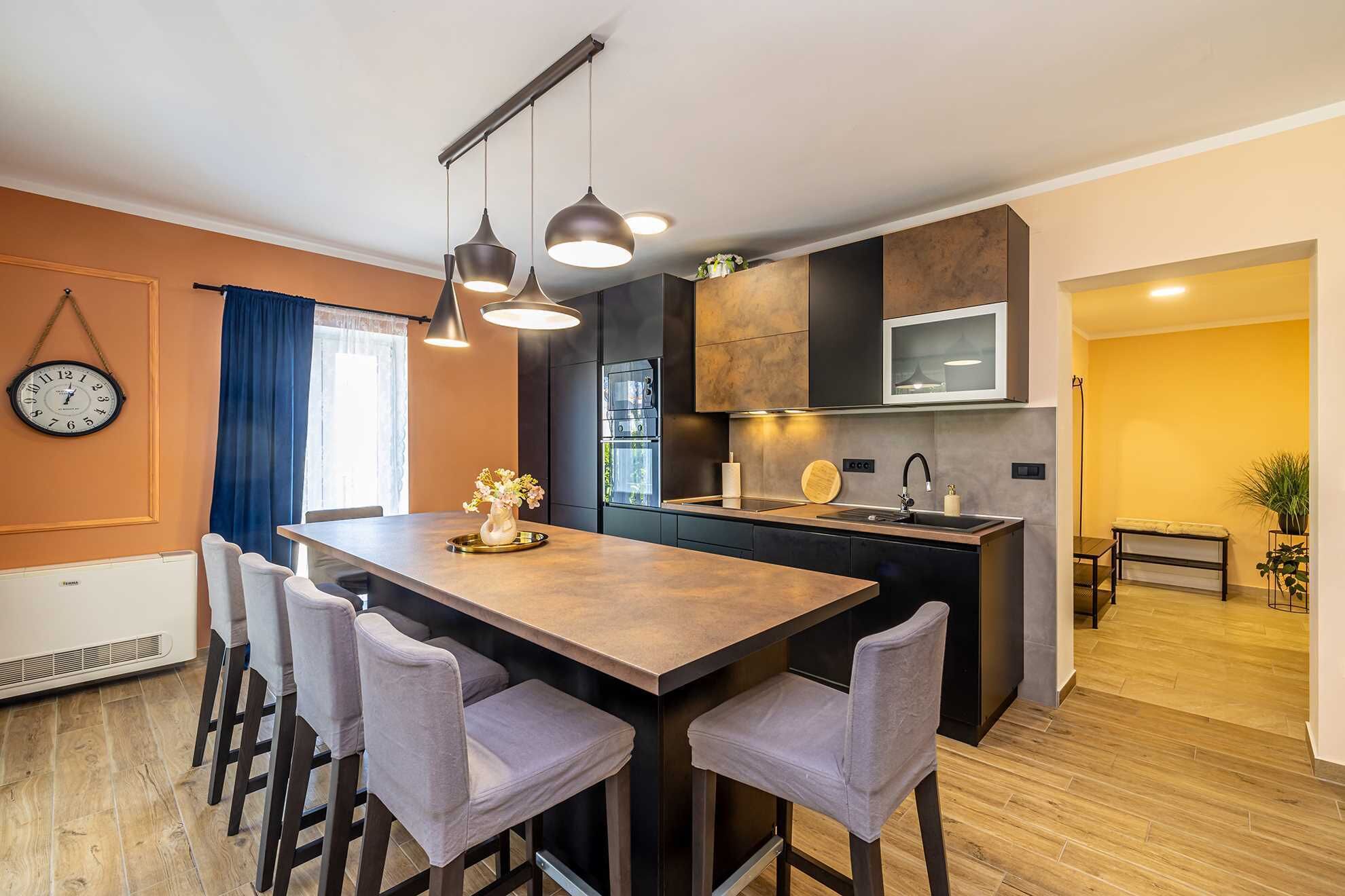 Een moderne keuken met een centraal eiland, barkrukken, hanglampen en een inbouwoven.