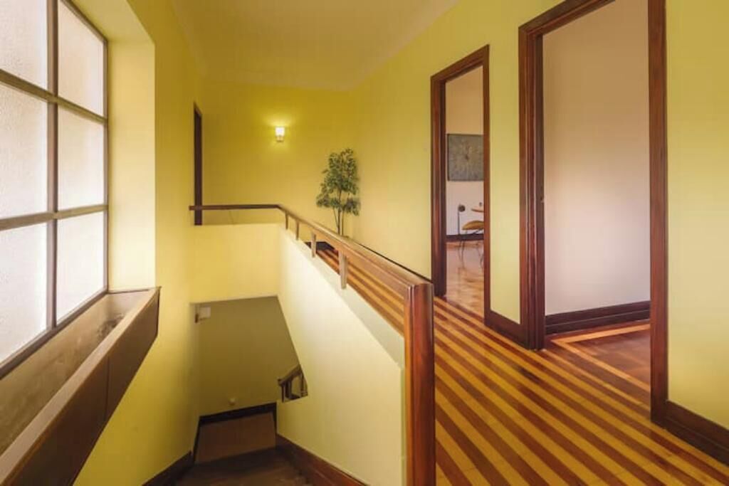 Un pasillo con barandilla de madera, una planta pequeña y un puerta al final.
