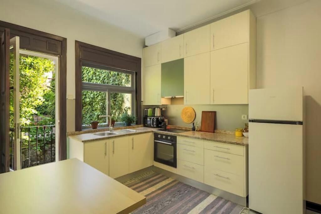 Una cocina con horno empotrado, refrigerador y ventana con vistas a la vegetación.