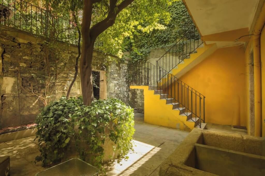 Un patio con una escalera que conduce a un nivel superior, rodeado de muros de piedra y follaje.