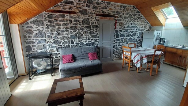 Ein gemütlicher Loftsraum mit Steinwand, grauem Sofa, Holzesstisch und einem kleinen Ventilator.