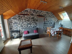 Ein gemütlicher Loftsraum mit Steinwand, grauem Sofa, Holzesstisch und einem kleinen Ventilator.