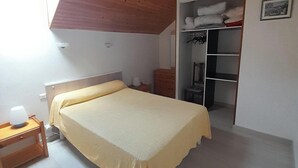 Ein Schlafzimmer mit Bett, Nachttisch, Kleiderschrank und einem kleinen Fenster.
