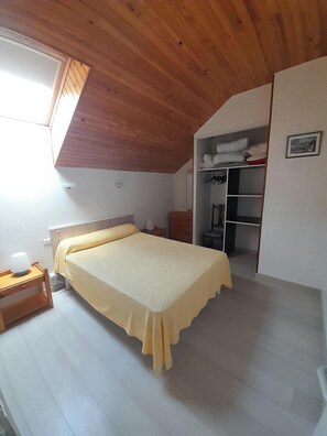 A bedroom with a bed, a nightstand, a bedside table, a wardrobe, and a small window. - One-Bedroom Apartment for Rent in the Heart of the Basque Country (Cambo-les-Bains)