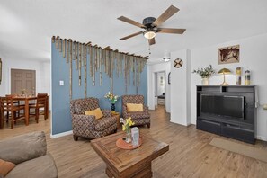 A living room with a ceiling fan, patterned armchairs, a coffee table with flowers, a fireplace, and a dining area with wooden furniture. - 2BR Apt Retreat Gated Downtown Killeen (Killeen)