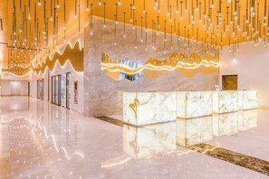 A modern lobby with a marble reception desk, hanging light fixtures, and a reflective floor.