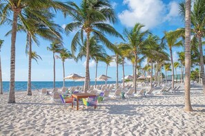 A beach with rows of palm trees, beach chairs, and umbrellas.