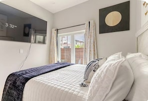 A bedroom with a bed, a window with curtains, a wall-mounted TV, and a circular artwork. - 2 Beds Near Downtown, Stockyards, Zoos, Sundance, 6 Flags,AT&T Stadium, Botanic (Fort Worth)
