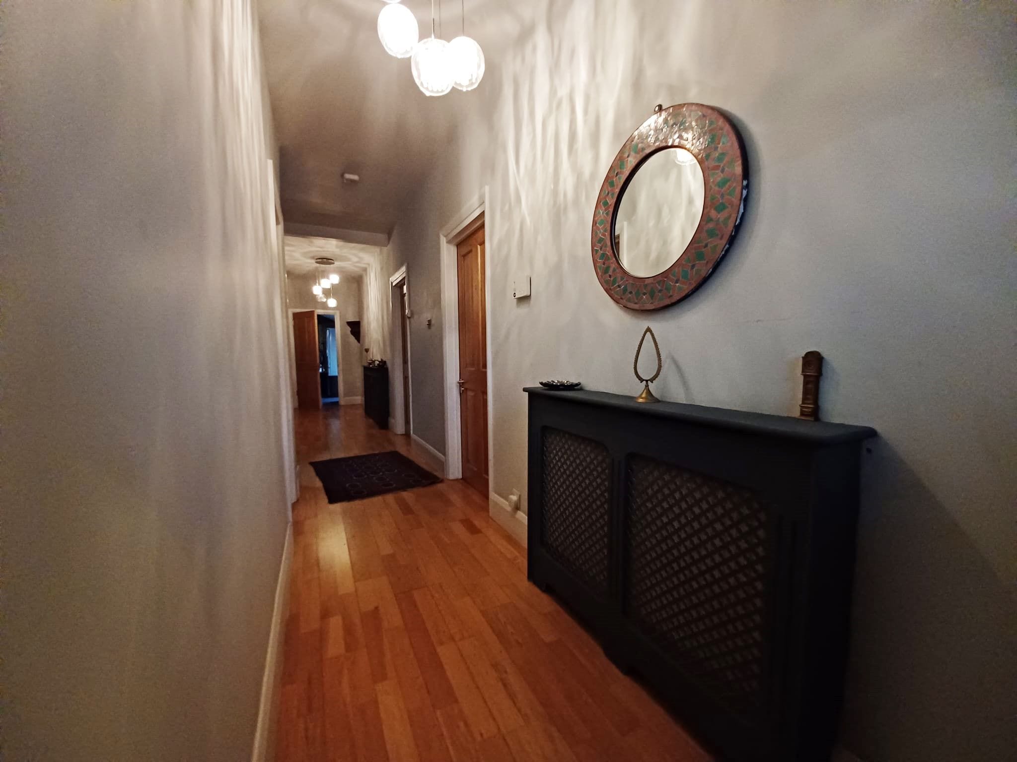A hallway with wooden flooring, a black console table, and a round mirror with a mosaic frame.