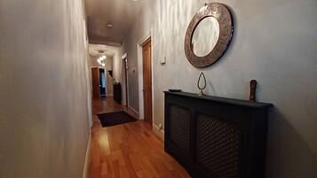 A hallway with wooden flooring, a black console table, and a round mirror with a mosaic frame.