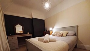 Et soveværelse med seng, sengebord, lampe og spejl.