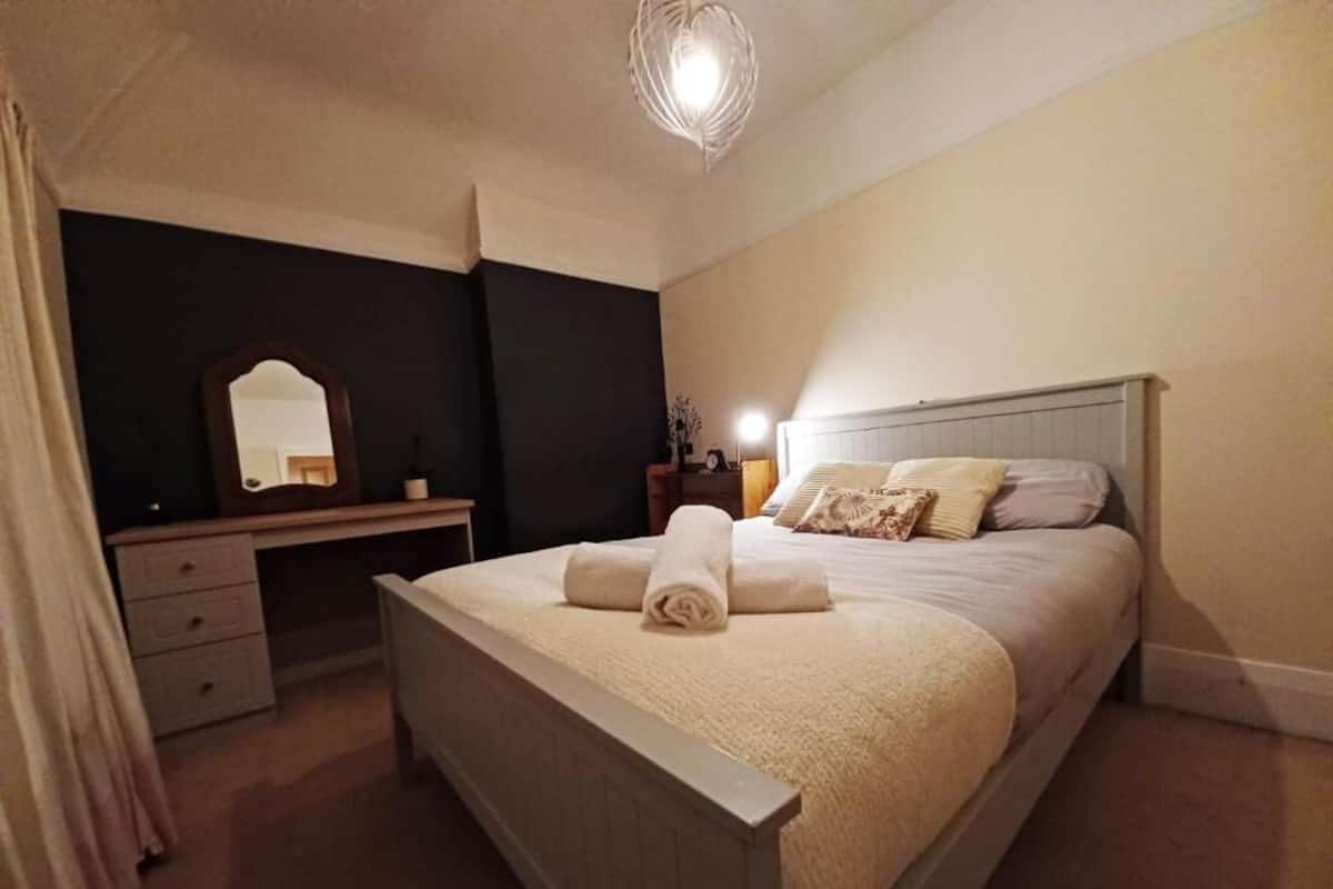 Een slaapkamer met een bed, nachtkastje, lamp en een spiegel.