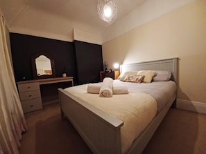 Een slaapkamer met een bed, nachtkastje, lamp en een spiegel.