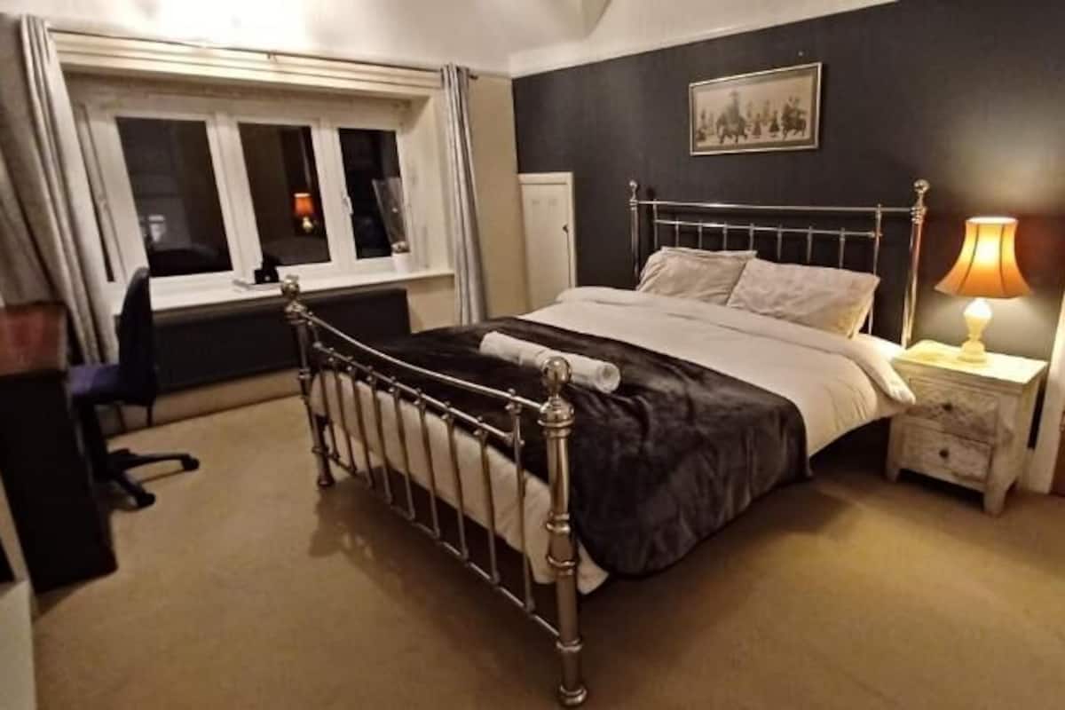 Een slaapkamer met een bed, nachtkastje, lamp, raam en een deur.