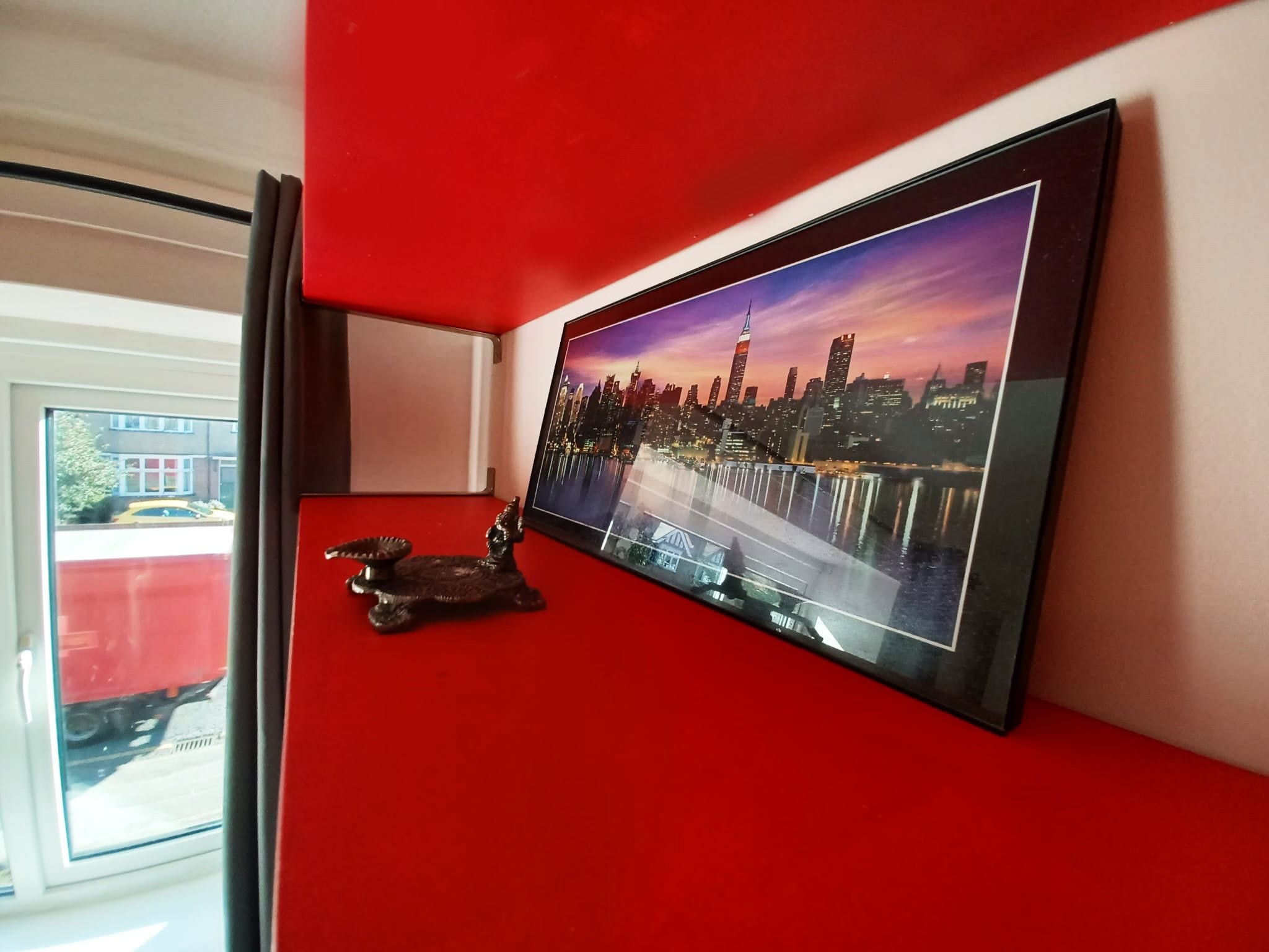 A flat-screen TV mounted on a red wall displaying a cityscape.