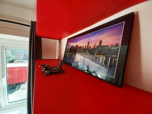 Ein Flachbildfernseher an einer roten Wand, der eine Stadtansicht zeigt.