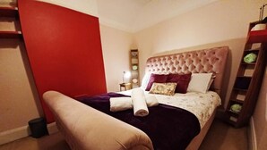 En pænt redt seng med en polstret sengegavl, et natbord med en lampe, og en rød væg.