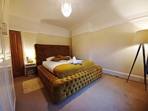 A bedroom with a large bed, a bedside table, a lamp, and a door. - The Gemstone Manor  (Watford)