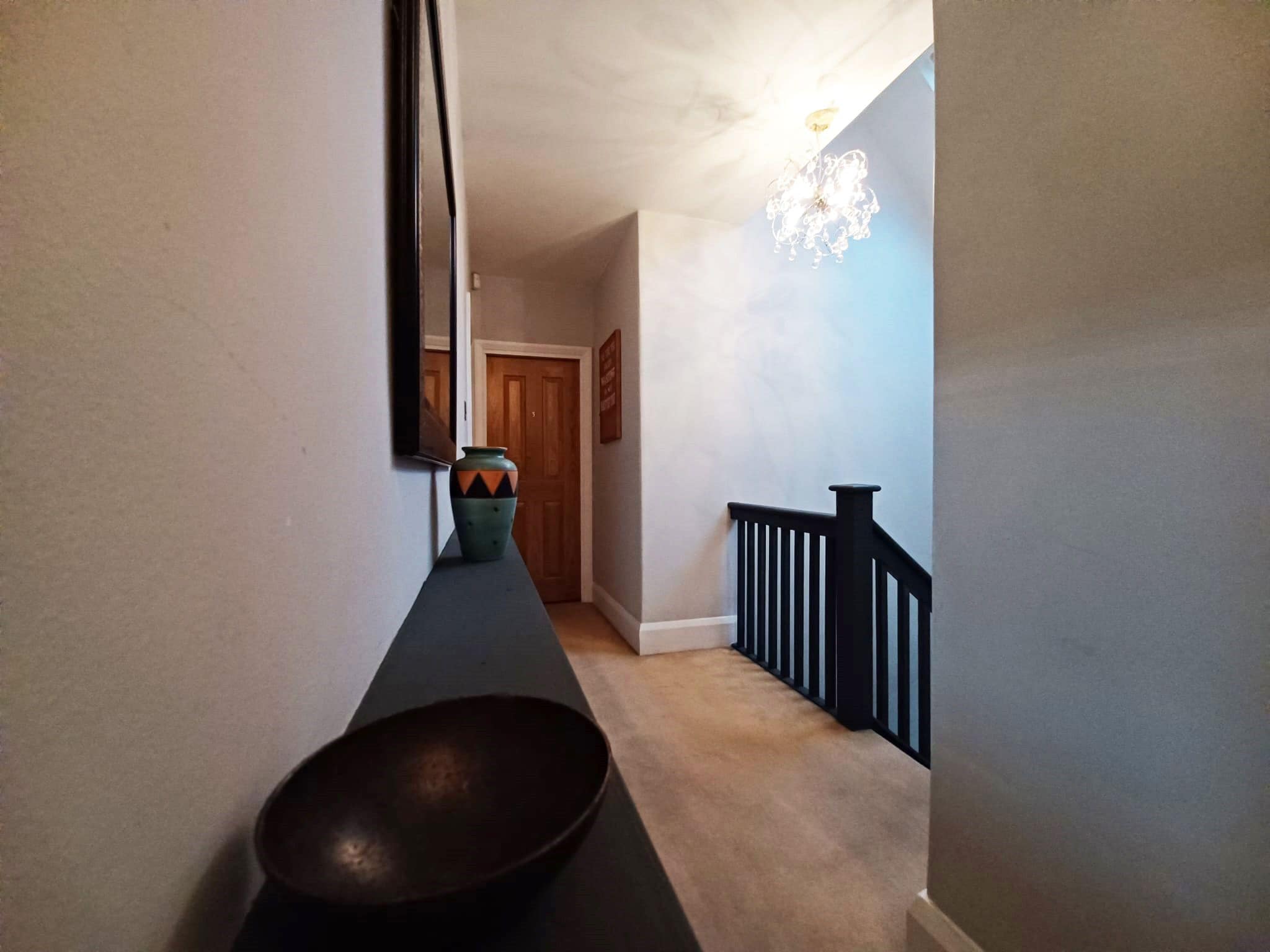 A hallway with a dark floor, a wall-mounted mirror, a decorative vase, and a door at the end.