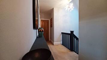A hallway with a dark floor, a wall-mounted mirror, a decorative vase, and a door at the end.