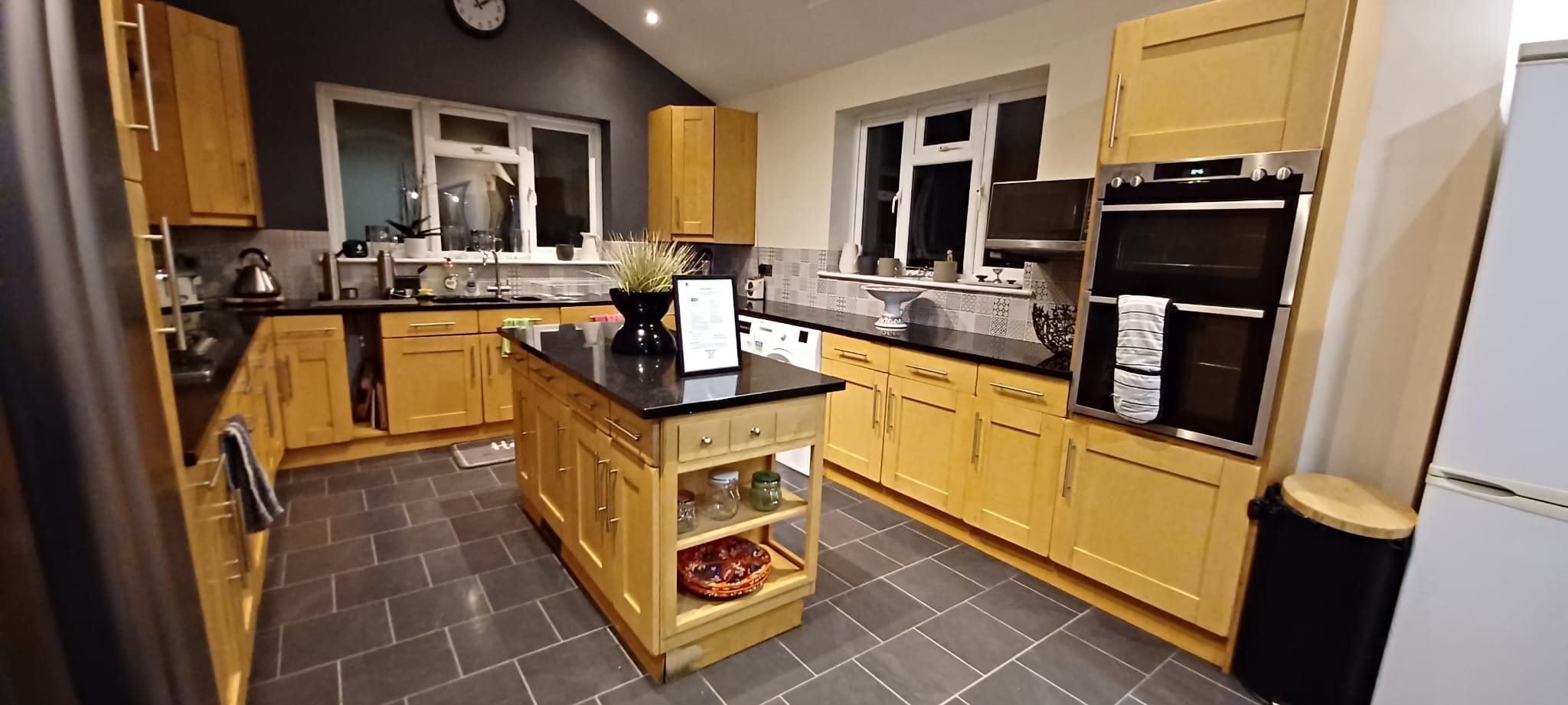 A modern kitchen with wooden cabinets, a black countertop, and a built-in oven.