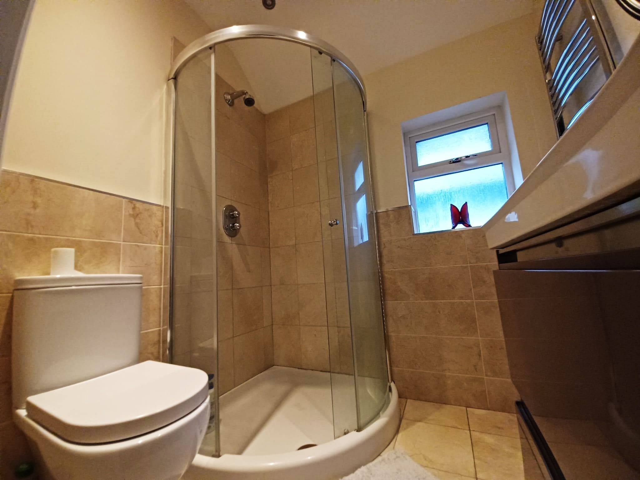 A bathroom with a glass-enclosed shower, a toilet, and a window with a butterfly decoration.