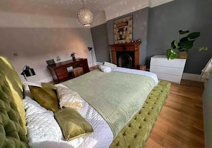 Een slaapkamer met een groot bed, een open haard, een bureau en een plant.