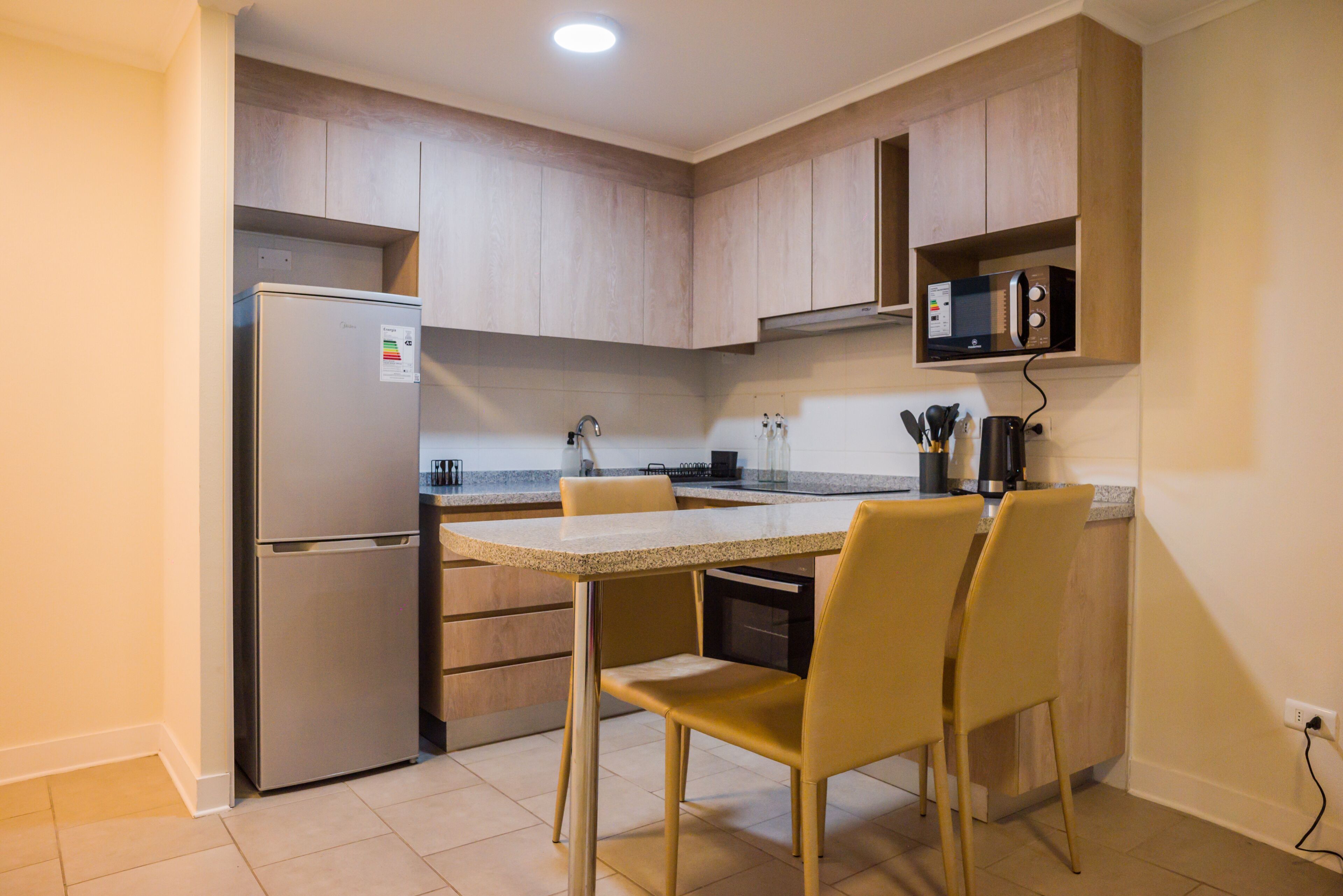 A compact kitchen with a built-in refrigerator, a microwave, and a dining area with chairs.