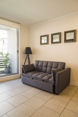 Ein Wohnzimmer mit grauem Sofa, einer Stehlampe und drei gerahmten Spiegeln an der Wand.