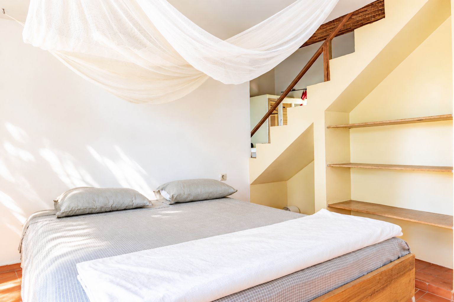 Quarto com cama, almofadas, cabeceira de madeira, escada e dossel branco.