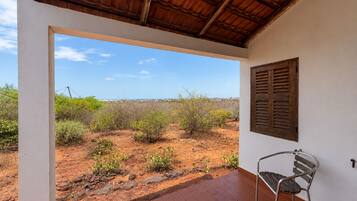 Una habitación con vista a un paisaje desértico, una ventana con contraventanas y una silla de metal.