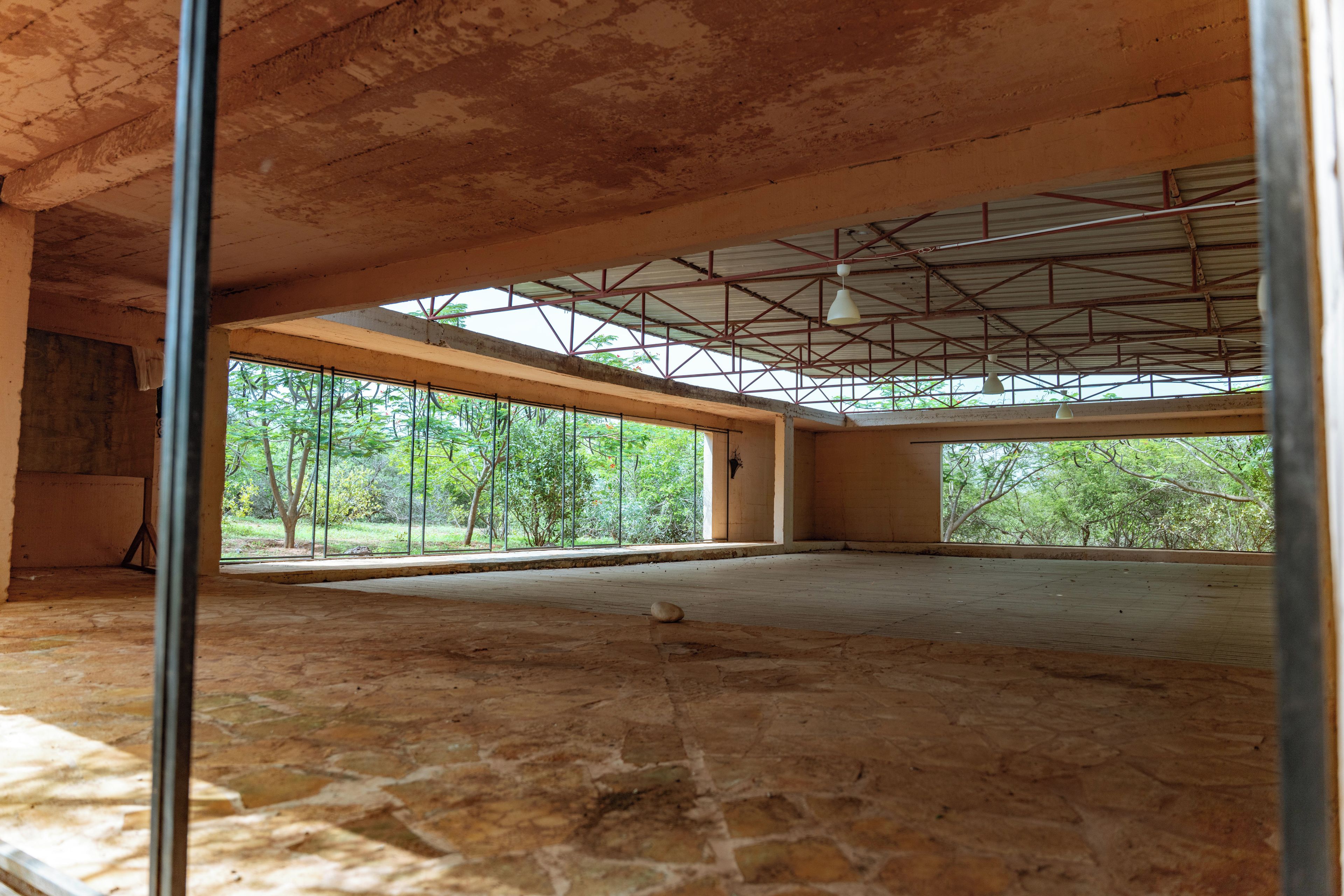 Un espacio interior con suelo de piedra, ventanas amplias y techo con estructura metálica.