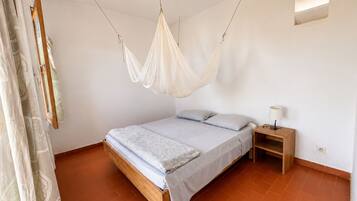 Un dormitorio con cama, mesita de noche, dosel colgante y ventana con persianas.