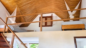 Ein Zimmer mit hohen Decken, Holzbalken, einem Bett mit weißer Bettdecke und einem Fenster mit Holzläden.