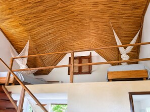 A room with a high ceiling, wooden beams, a bed with a white bedspread, and a window with wooden shutters.