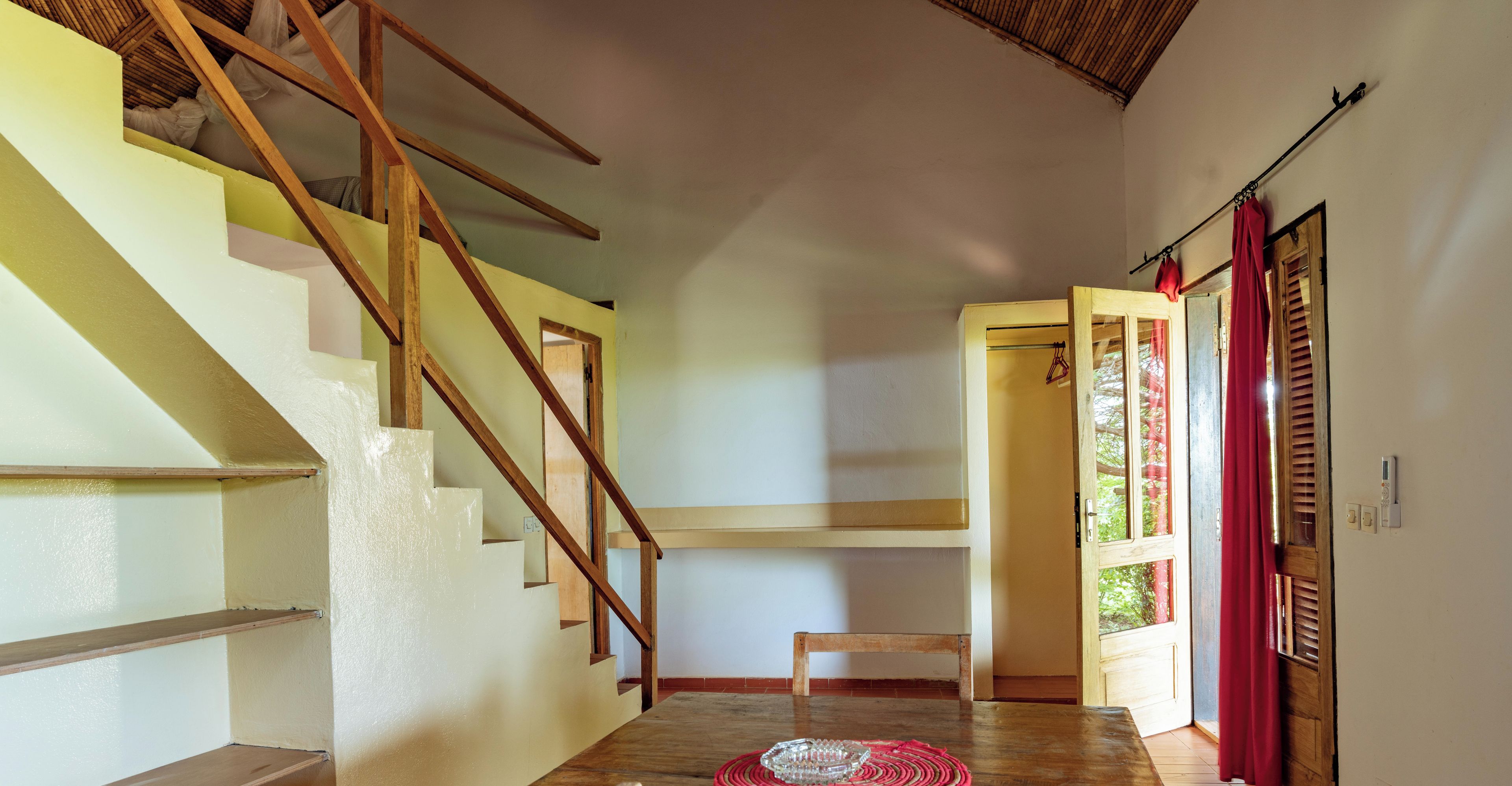 A staircase leading to a second floor, a wooden bench, and a door with a red curtain.