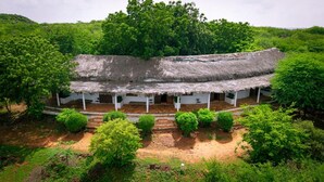 Ein traditionelles Gebäude mit einem Reetdach und einer Veranda, umgeben von üppiger Vegetation.