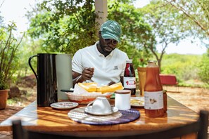 A person sitting at an outdoor table with a meal, a bottle, and a jug. - Mampuya (Popenguine)