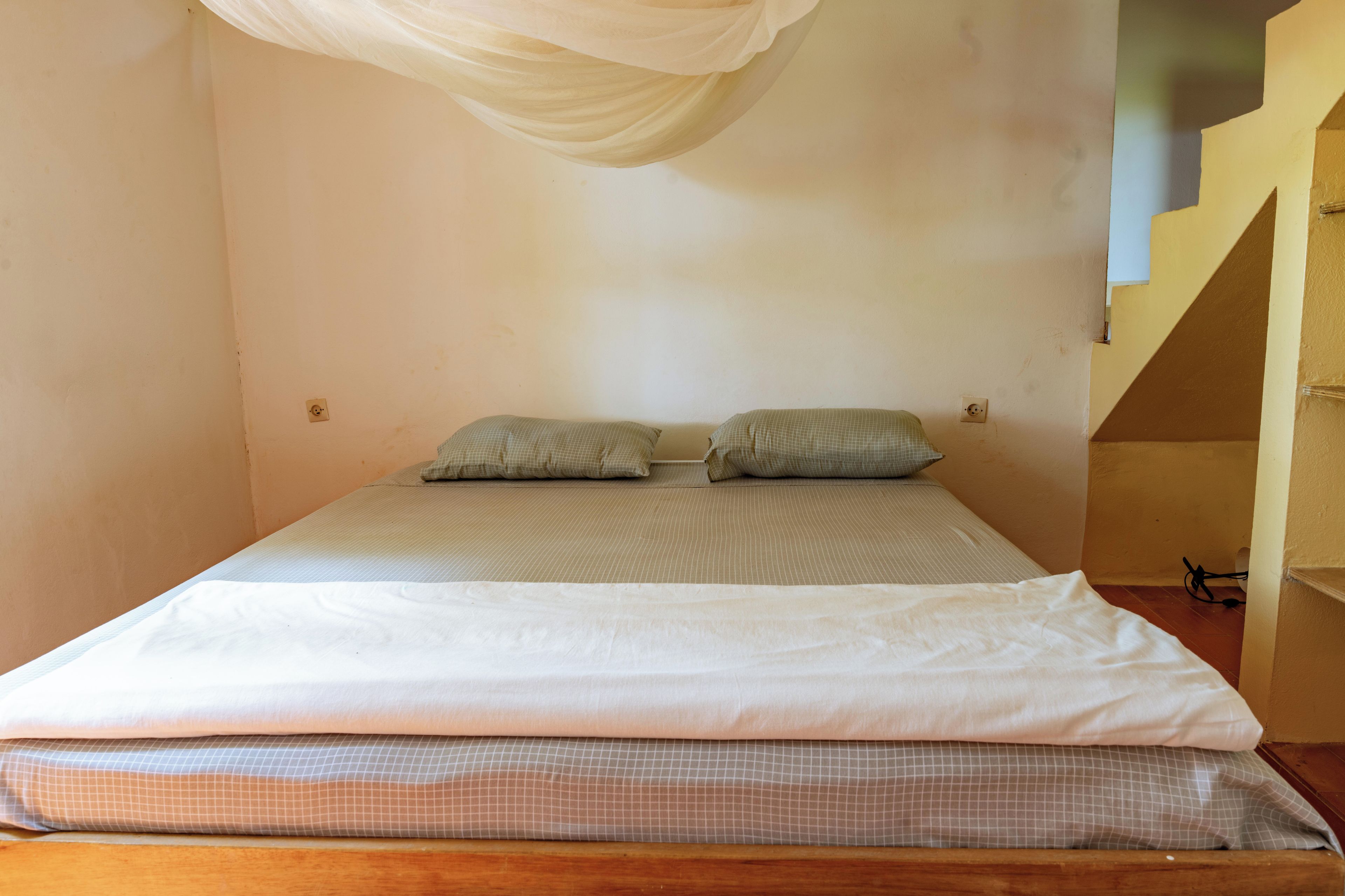 Ein Einzelbett mit einer Matratze und Kissen in einem Raum mit schlichten Wänden und einer schrägen Decke.