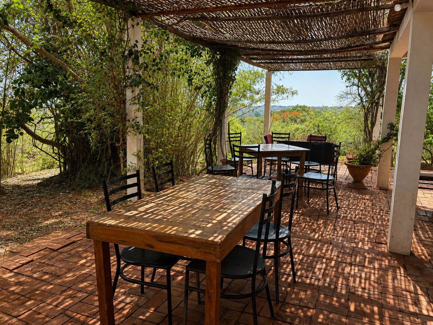 An outdoor patio with a wooden table and chairs, surrounded by greenery and a view of the landscape.