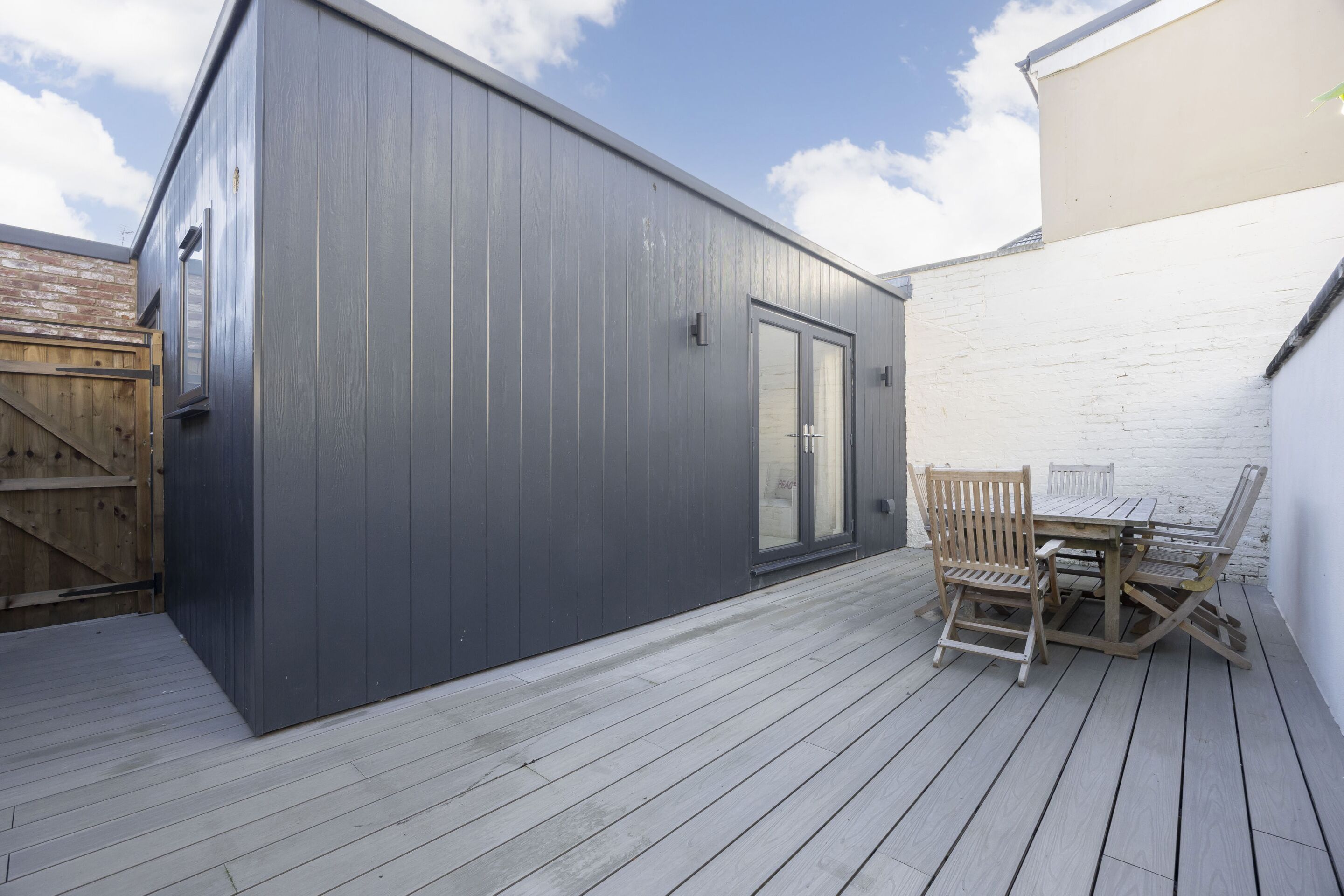 A modern building with a dark exterior, a wooden deck, and a table with chairs.