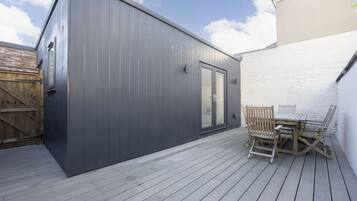 A modern building with a dark exterior, a wooden deck, and a table with chairs.