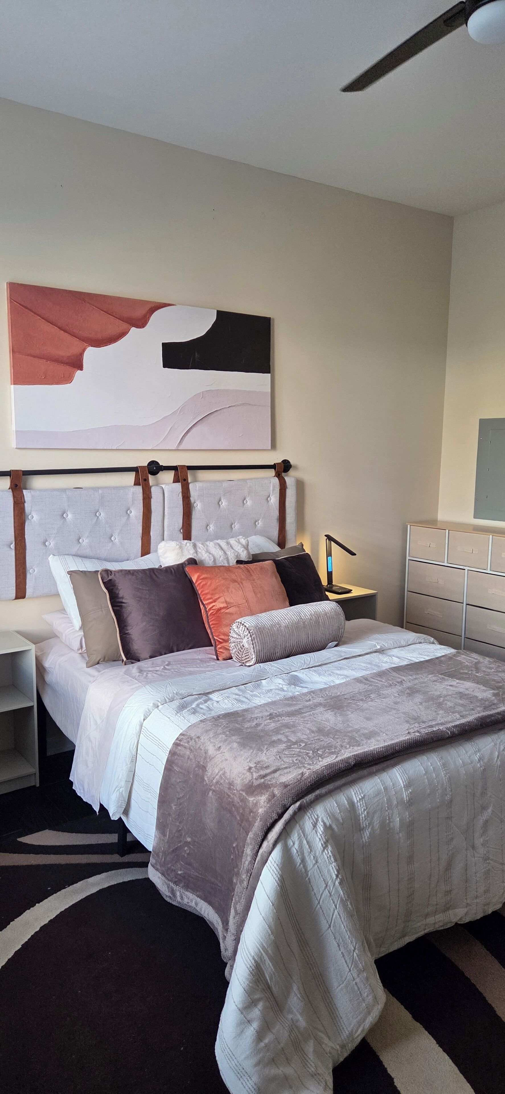 A bedroom with a bed, a nightstand, a lamp, a dresser, and a ceiling fan.
